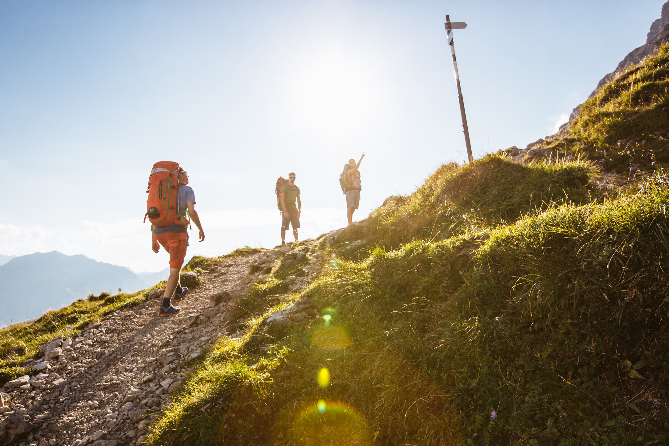 Wanderer auf Höhenweg im Gegenlicht der Abendsonne in den Alpen.